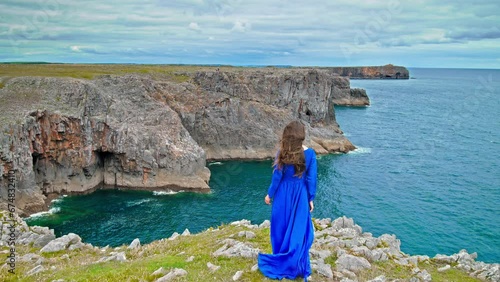 Tourist girl standing on a cliff enjoying the view of the Pembrokeshire Coast National Park. A beautiful woman enjoying turquoise water coastal walks, watersports, scenic beaches and coves in Wales. photo