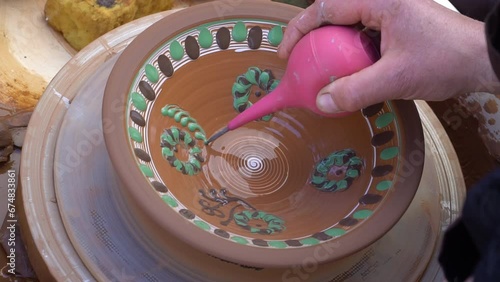 Close up real time shot of hands painting  ukrainian pattern on glased  clay plate. photo