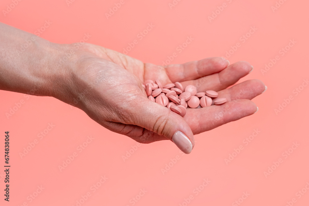 Many pink pills in woman hand on pink background. Medical concept of medicine treatment, vitamins, supplements, contraceptive pills or feminine drug addiction. Selective focus