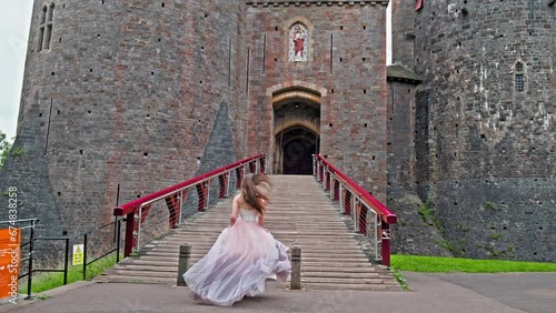 A beautiful woman in a princess long dress visits Red Castell Coch with great towers and conical roofs in Cardiff, Wales. Tourist girl enjoys the gothic-revival style with ancient beech woods in Wales photo
