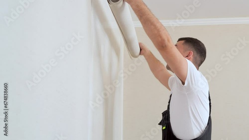 Worker attaching wallpaper to wall. One strip of new wallpaper wrapped in a roll. Slow motion 4k