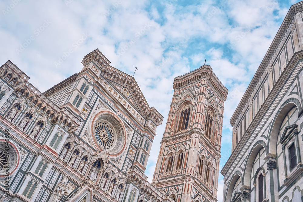 Detail of the facade of the Basilica Santa Maria del Fiore and Giotto's bell tower with space above on blue sky and clouds, on the right the Baptistery of San Giovanni