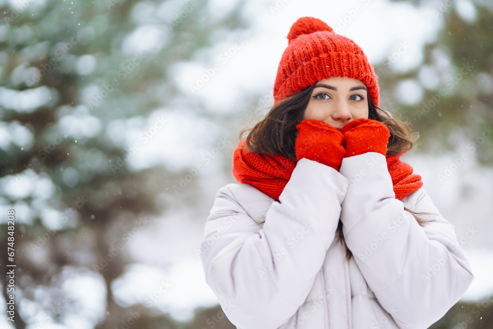 Obraz premium Portrait of a beautiful woman in a red hat in a snowy forest. Young woman having fun with snow on a winter day. Vacation concept, nature.