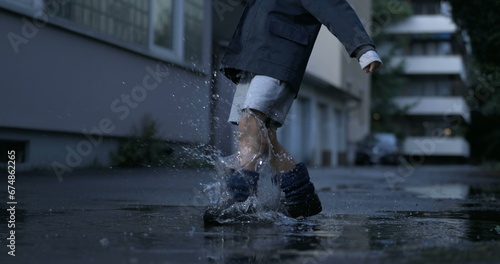 Nostalgic scene of child kicking puddle of water in street alley having fun by himself filmed in high-speed camera