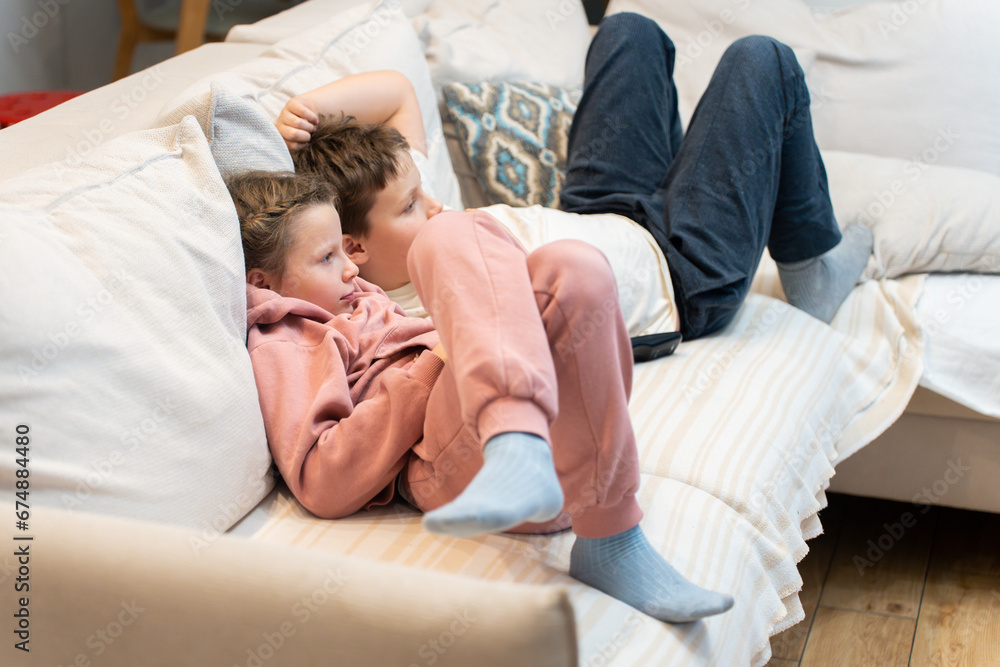 Brother and sister lying comfotable sofa and waching TV exciting movie. Common interests among children. Joint rest after school day.
