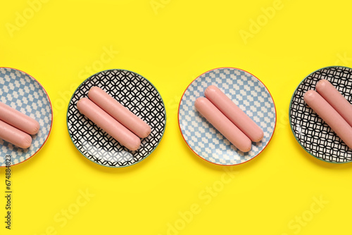 Plates with tasty thin sausages on yellow background