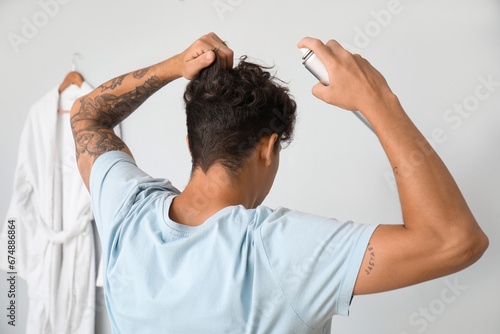 Konstfotografi Handsome young man with tattoo applying hair spray on his curly hair in bathroom