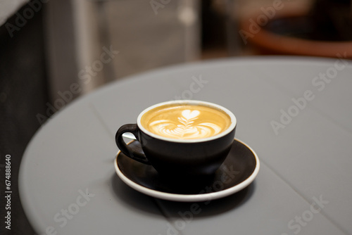 Black cup of fresh cappuccino with latte art on gray metal table background. Empty place for text, copy space. Coffee addiction concept. Hot drinks beverage