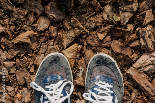 A poor man in old torn suede sneakers with holes stands on dry leaves in the forest in autumn. Photography, nature walk.