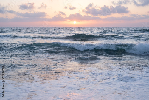 sun sets on a dramatic cloudy sky over the Mediterranean Sea horizon with a warm, golden glow. The sea's waves magical tranquil seascape