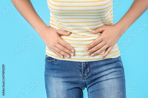 Young beautiful woman suffering from abdominal pain on blue background, closeup © Pixel-Shot