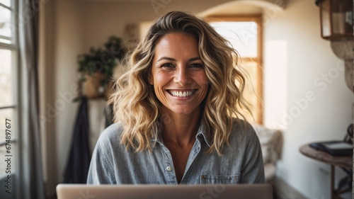 Spontaneous mature woman, smiling looking at camera working on a laptop in the comfort of her home, Senior adult woman writer using laptop photo