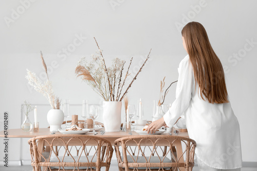 Beautiful woman setting table with dried flowers in dining room © Pixel-Shot