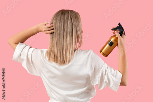 Young blonde woman with hair spray on pink background, back view photo