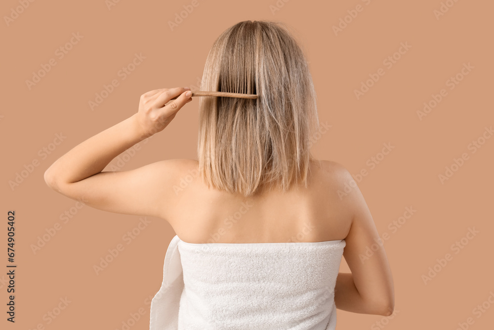 Young blonde woman combing hair after shower on beige background, back view Young blonde woman combing hair after shower on beige background, back view