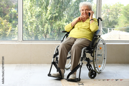 Senior woman in wheelchair talking by mobile phone at home