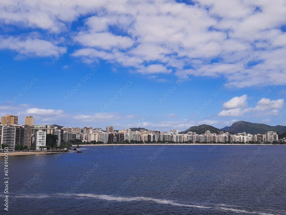 View of Icaraí Beach in Niterói, Rio de Janeiro, Brazil, tall buildings, calm waters of Guanabara Bay and blue sky with clouds on a spring afternoon