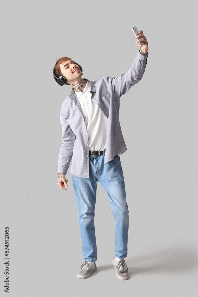 Happy young man in headphones taking selfie on grey background Happy young man in headphones taking selfie on grey background