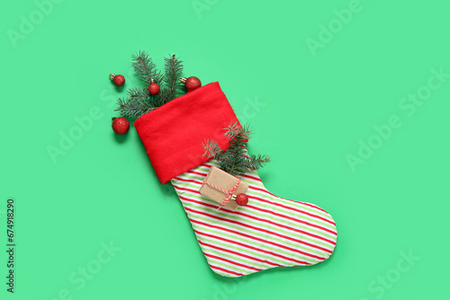 Christmas sock with fir branches, balls and gift box on green background photo