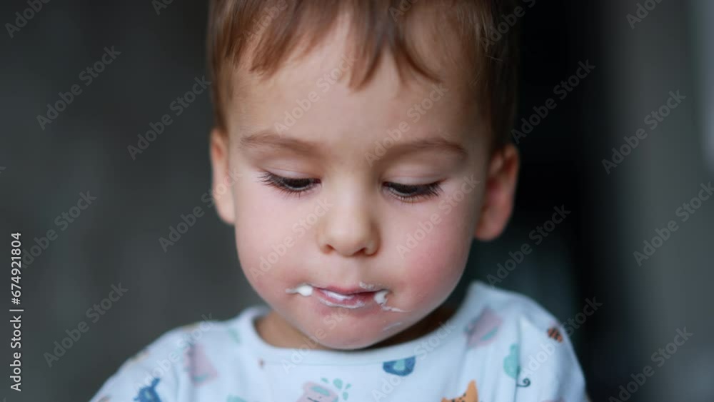 Charming baby boy with dairy around his mouth. Face of a kid eating yogurt from spoon. Close up. Charming baby boy with dairy around his mouth. Face of a kid eating yogurt from spoon. Close up.