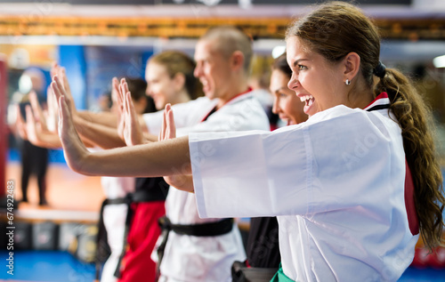 Closeup portrait of emotional young girl in kimono practicing basic martial arts techniques during group self defense training in gym