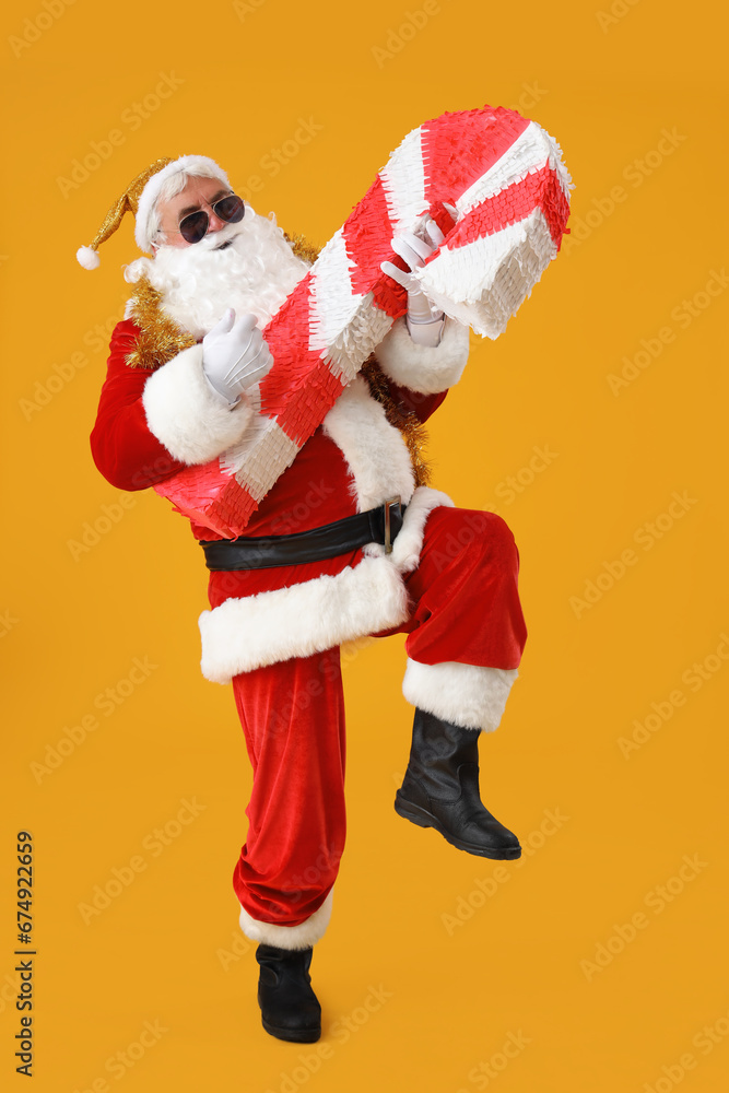 Cool Santa Claus with candy cane pinata on yellow background