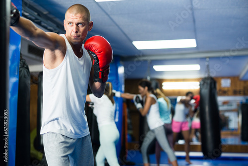 Man and women in boxing gloves exercising jabs on punchbags in gym.