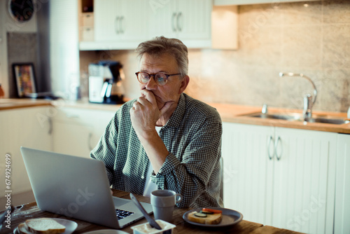 Middle aged man using laptop on kitchen table photo