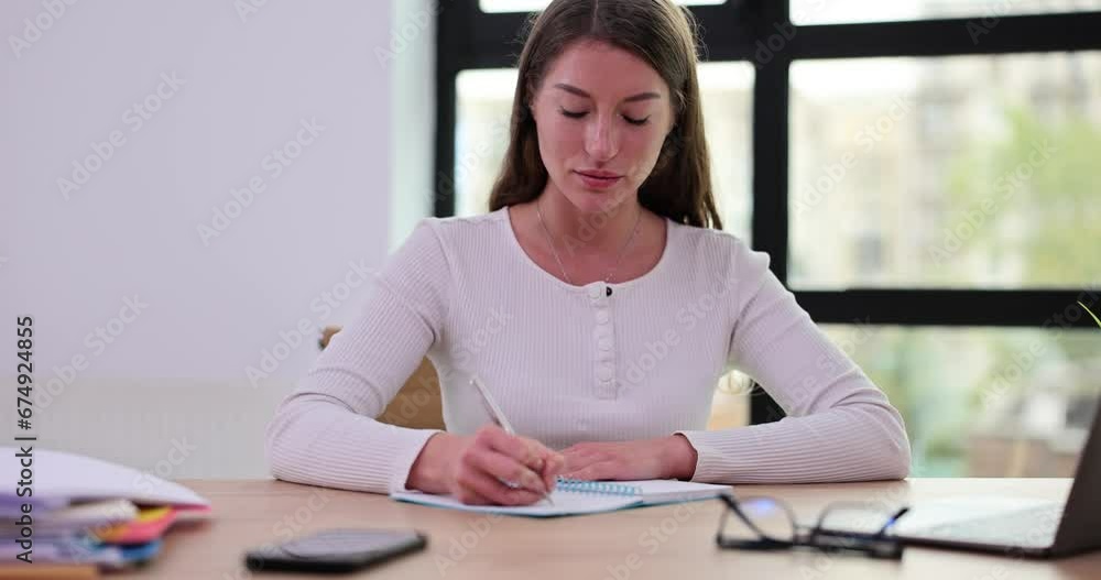 Woman manager is sitting at desk at workplace and making notes in notepad Woman manager is sitting at desk at workplace and making notes in notepad