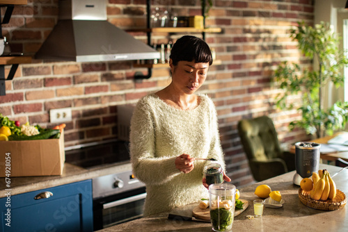 Woman is preparing a healthy detox drink in a blender in kitchen photo