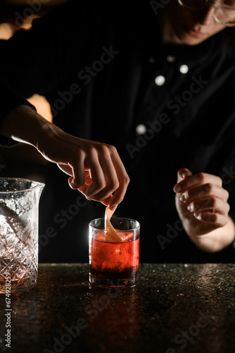 Female bartender dips a piece of orange peel into a glass with a cocktail