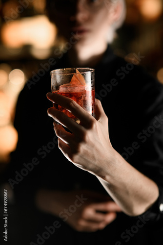 Female hand holds a glass filled with iced cocktail and a piece of orange peel