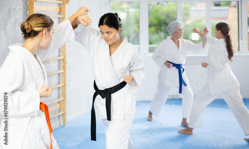 Two young women practicing self-defense techniques in group at gym