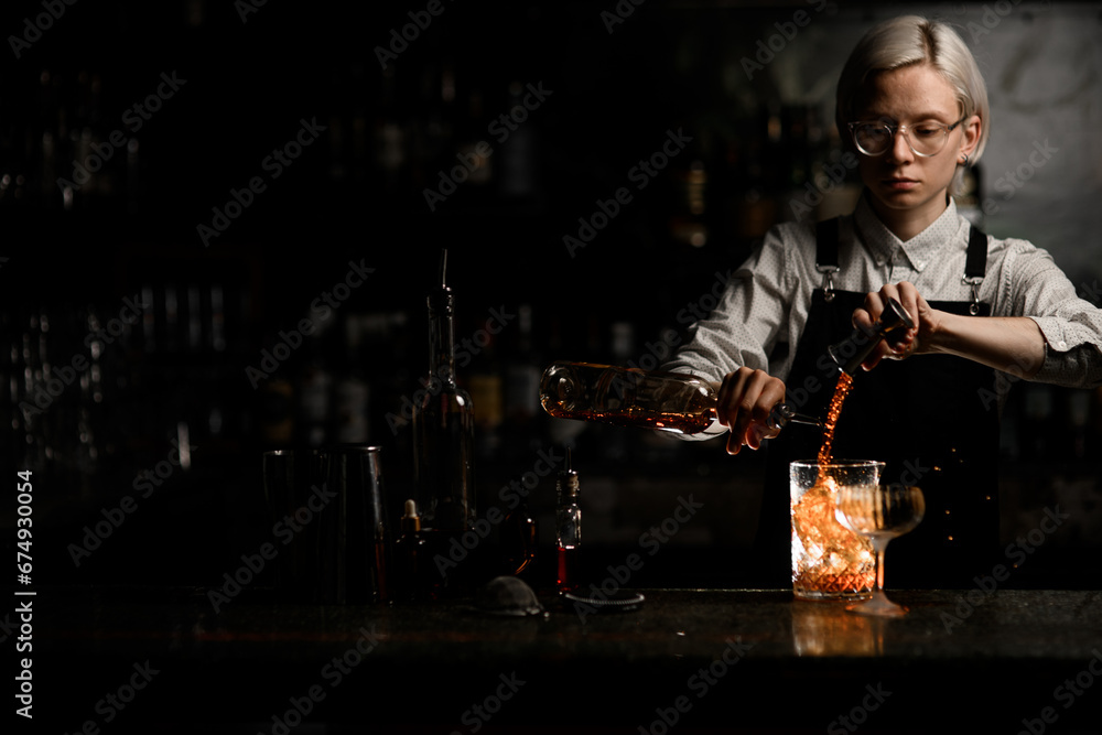 Female bartender is concentrating on preparing an alcoholic cocktail in a mixing glass with ice