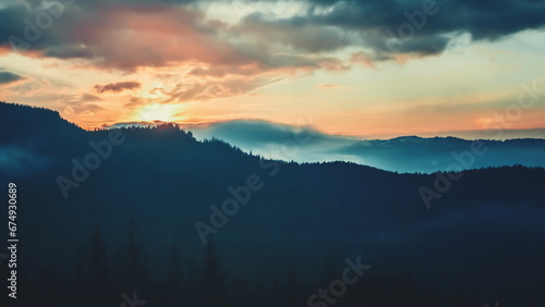 Epic foggy colorful sunrise in alp mountains. Dramatic clouds flow in bright sky, sun glow rising over mountain peak with golden light beams. Beautiful morning nature landscape.