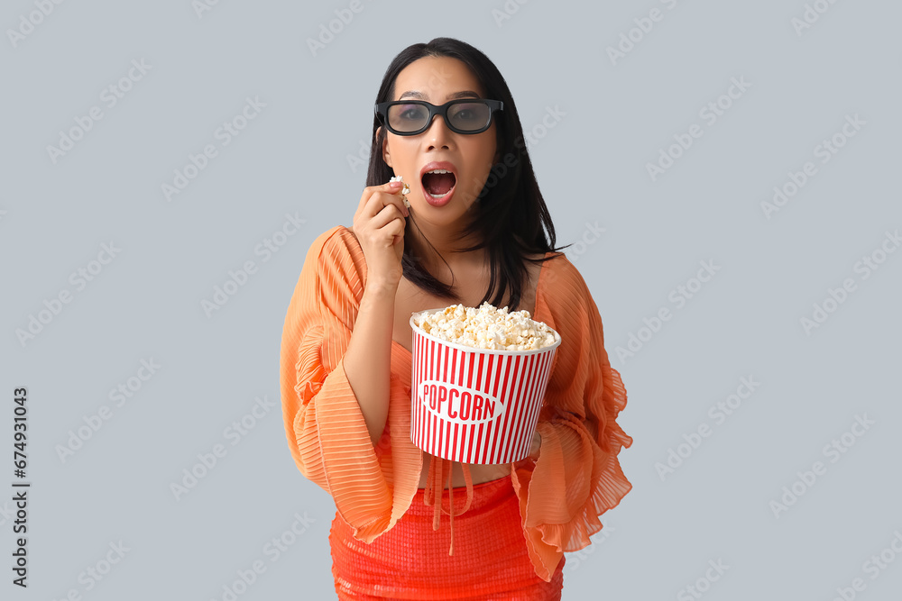 Young Asian woman in 3D glasses with bucket of popcorn on white background