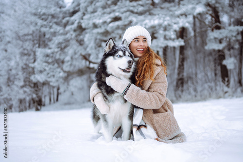 A cheerful husky dog walks with its owner in a snowy forest. A young woman with her pet on an adventure. Friendship concept, pets. © maxbelchenko