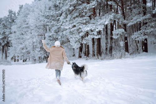 A cheerful husky dog walks with its owner in a snowy forest. A young woman with her pet on an adventure. Friendship concept, pets.