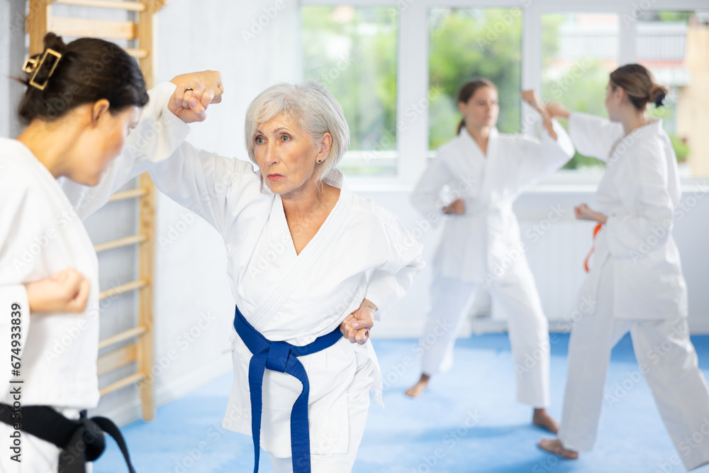 Women in white kimonos are engaged in wrestling at sports training. Woman paired up with female partner performs classic techniques of repelling blow in karate technique