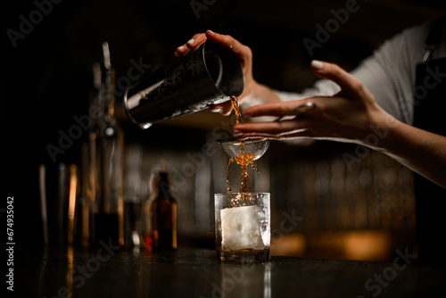 Female hand pours a cocktail through a strainer from a metal tumbler into a glas Fototapeta