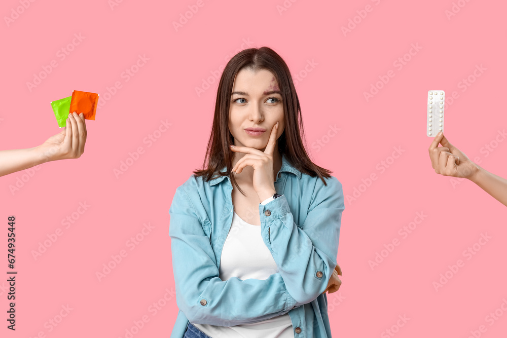 Beautiful young woman and hands holding contraceptive pills and condoms on pink background. Beautiful young woman and hands holding contraceptive pills and condoms on pink background.