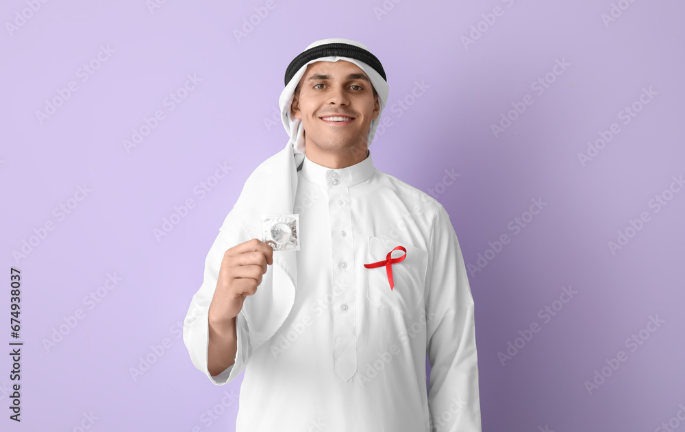 Handsome Muslim man with red ribbon and condom on purple background. AID awareness concept Handsome Muslim man with red ribbon and condom on purple background. AID awareness concept