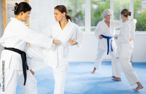 Focused young woman in white kimono practicing knee strike technique during sparring with female opponent at karate training ..