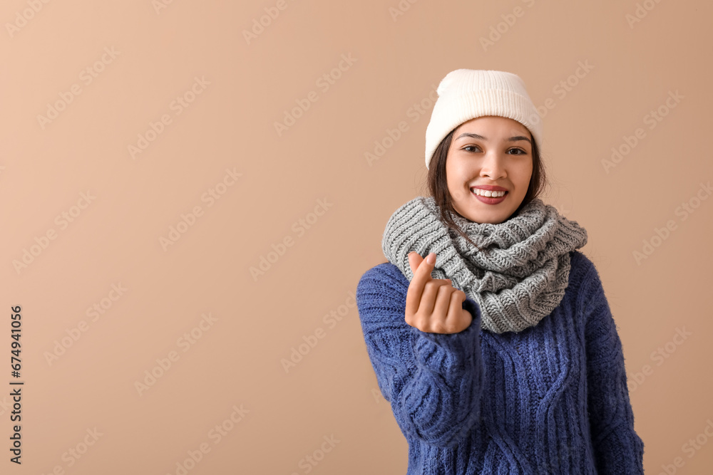 Beautiful young Asian woman in warm scarf showing heart gesture on brown background Beautiful young Asian woman in warm scarf showing heart gesture on brown background