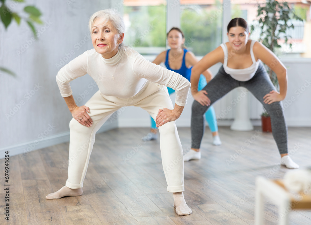 Obraz premium Sporty motivated young elderly women warming up with energetic dances before strength training in gym studio