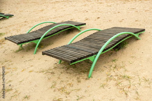 two wooden sun loungers in autumn on the beach near the lake on light sand photo