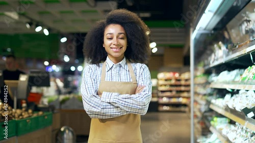 Portrait of a saleswoman female worker in a supermarket looking at camera and smiling. African american black woman employee clerk in apron in grocery store Happy Positive greengrocer girl in market photo