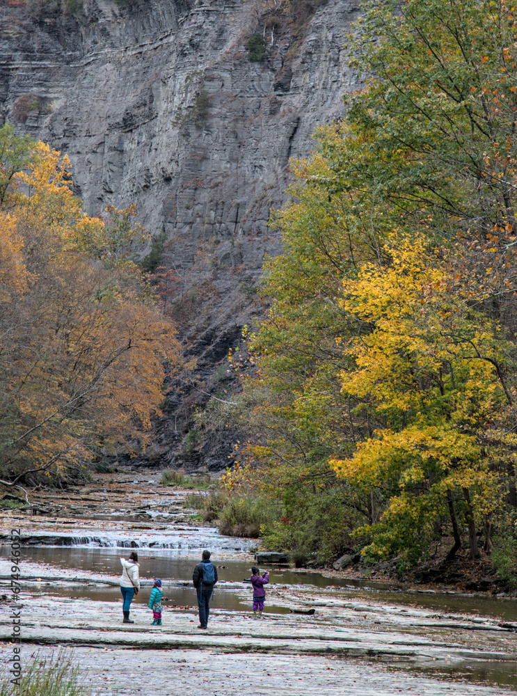 family walking inside gorge at Taughannock Falls State Park, a tourist destination in the Finger Lakes region of upstate New York. Famous waterfall in autumn with leaves changing color, foliage. family walking inside gorge at Taughannock Falls State Park, a tourist destination in the Finger Lakes region of upstate New York. Famous waterfall in autumn with leaves changing color, foliage.