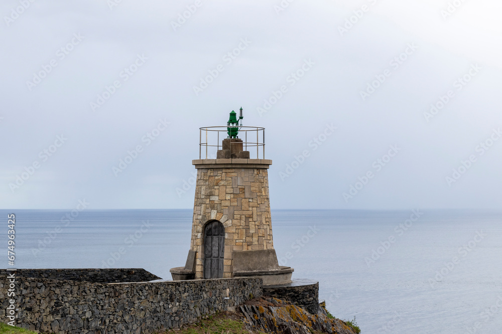a stone lighthouse with a green statue on top, overlooking the calm ocean under an overcast sky