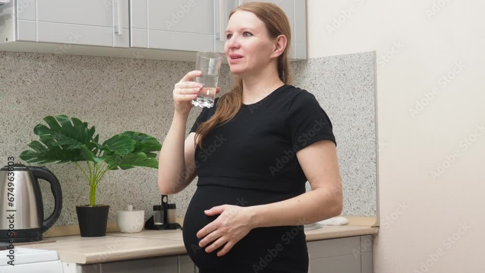 Pensive pregnant woman drinking water in the kitchen. Young happy expectant thinking about her baby and enjoying her future life. Motherhood, pregnancy Pensive pregnant woman drinking water in the kitchen. Young happy expectant thinking about her baby and enjoying her future life. Motherhood, pregnancy